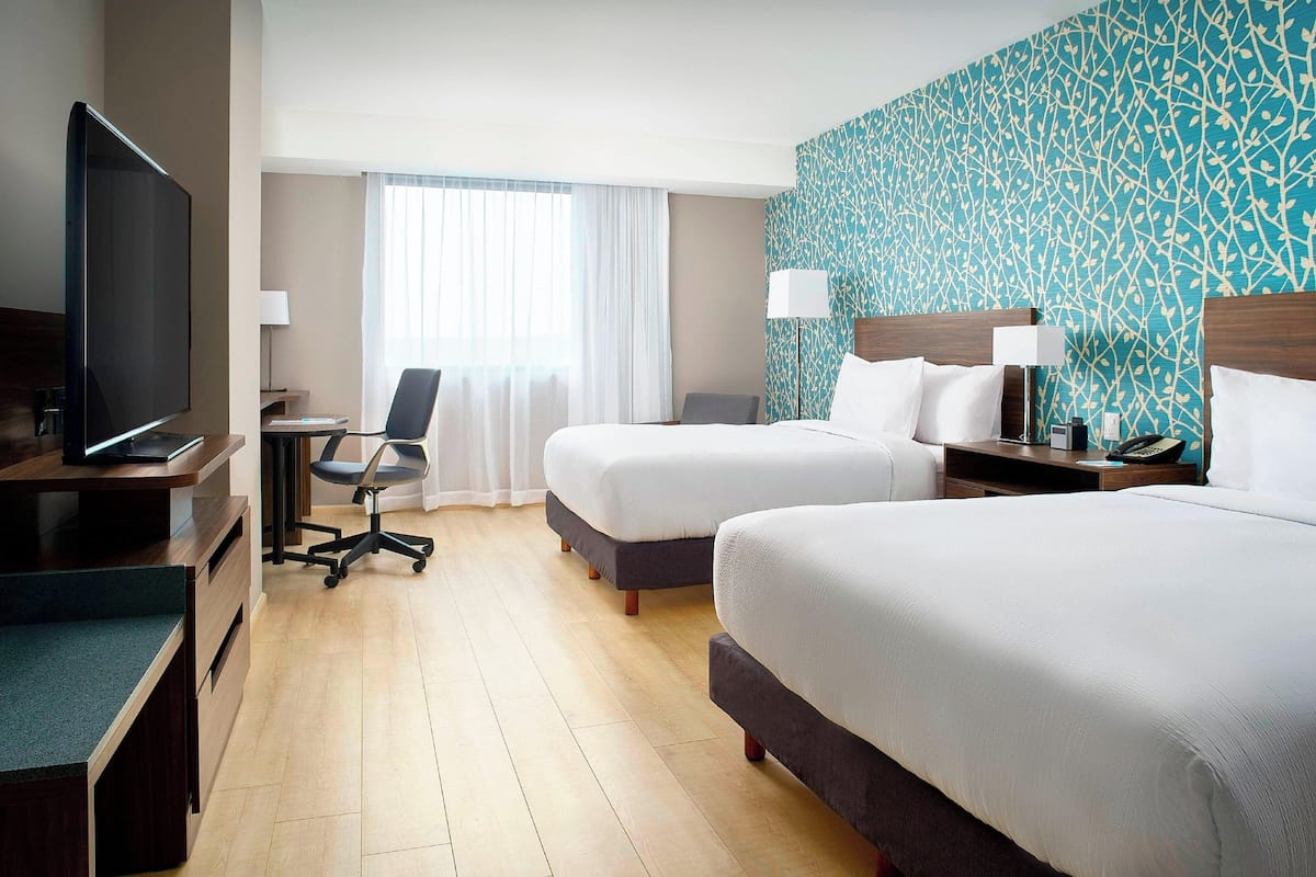 A hotel room with two beds, a desk with a computer, a TV, and a window with curtains.