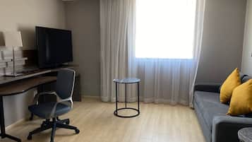 A modern living room with a desk, chair, TV, and a sofa with cushions.