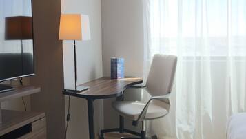 A hotel room with a desk, chair, lamp, and a television.