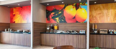 A modern kitchen with wooden cabinets, a black countertop, and a large fruit mural on the wall.
