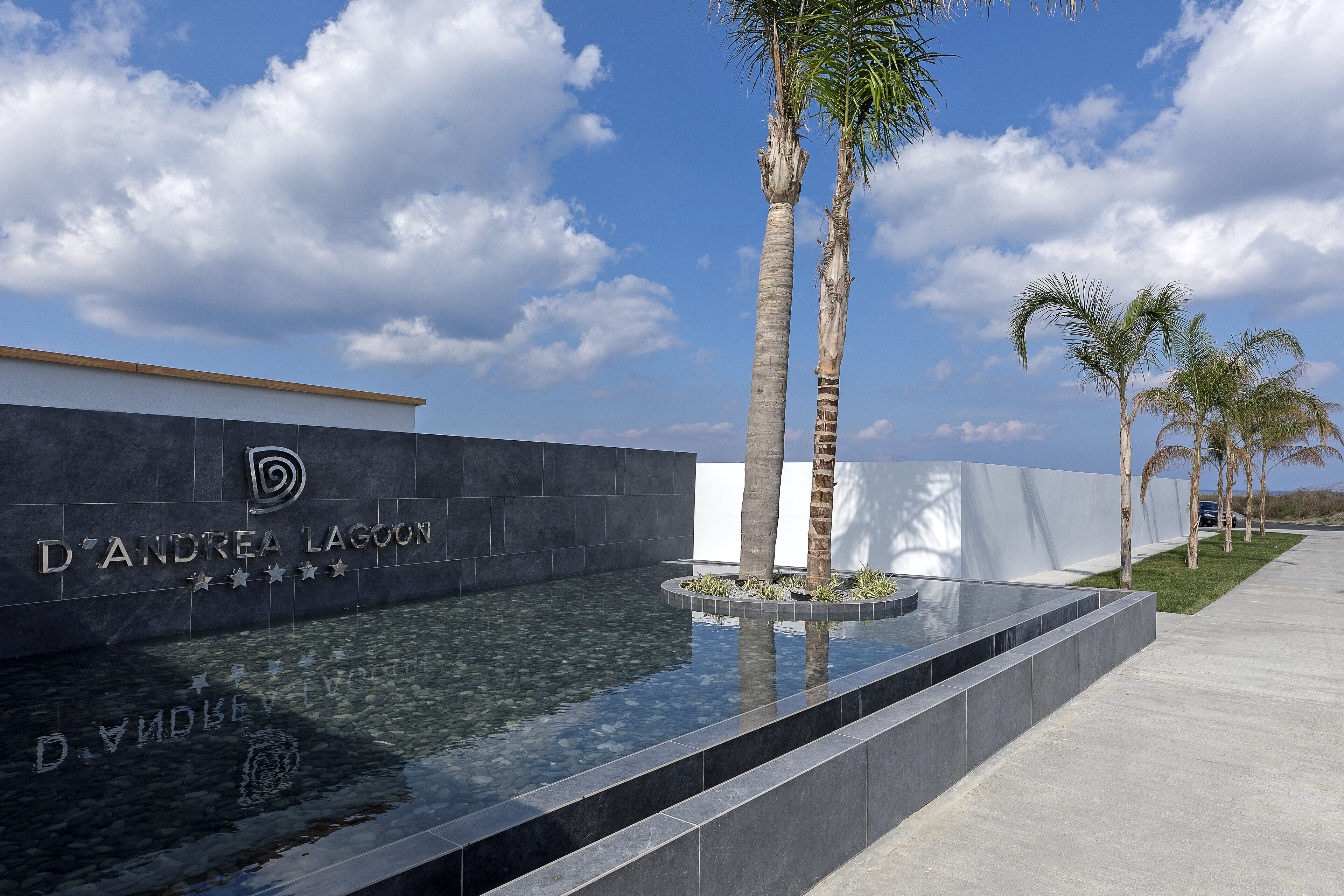 A modern building with a clear pool, palm trees, and a sign reading "D'Andrea Lagoon."