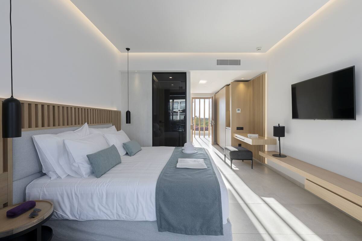 A modern hotel room with a large bed, bedside table, and a TV mounted on the wall.