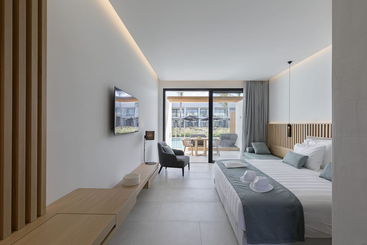 A modern hotel room with a large bed, a desk, and a view of the outdoor area.