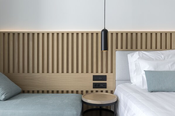Una habitación de hotel moderna con un cabecero de listones de madera, una mesita auxiliar redonda de madera y una cama con ropa blanca.