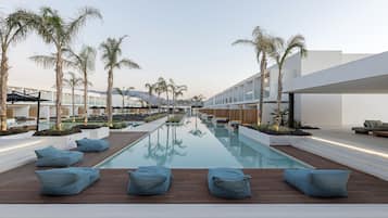 A modern pool area with wooden decking, blue bean bags, and palm trees.