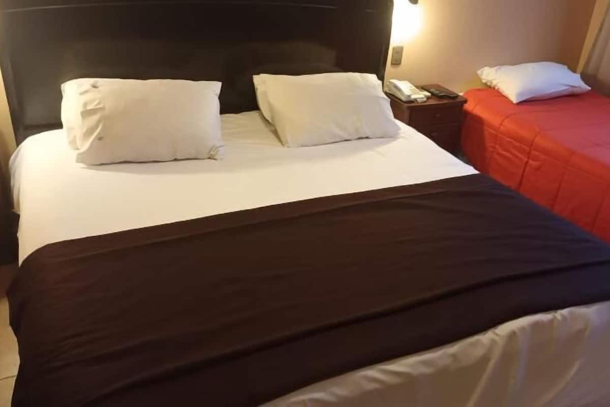 Una habitación de hotel con una cama grande, una cama más pequeña y una mesita de noche con un teléfono.
