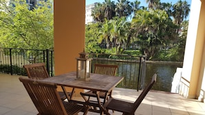 A wooden table and chairs on a tiled patio with a view of a water body and greenery. - Luxurious Apartment in Century City (Cape Town)