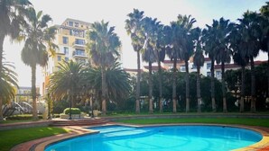 A swimming pool surrounded by palm trees and a building with multiple balconies. - Luxurious Apartment in Century City (Cape Town)