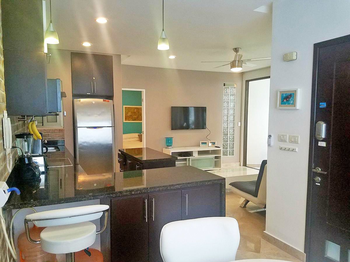 A modern kitchen with a refrigerator, stove, and dining area. There is a TV mounted on the wall and a window providing natural light.