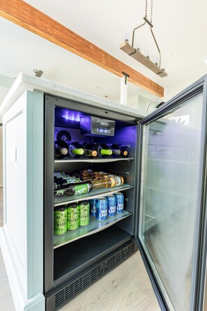 Mini-geladeira com diversas bebidas, incluindo cerveja e refrigerantes, em um quarto com vigas de madeira no teto.