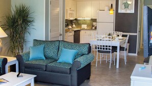 A living room with a sofa, a dining table with chairs, a kitchen area with cabinets and appliances, and a ceiling fan. - Club Wyndham Grand Palms (Surfside Beach)