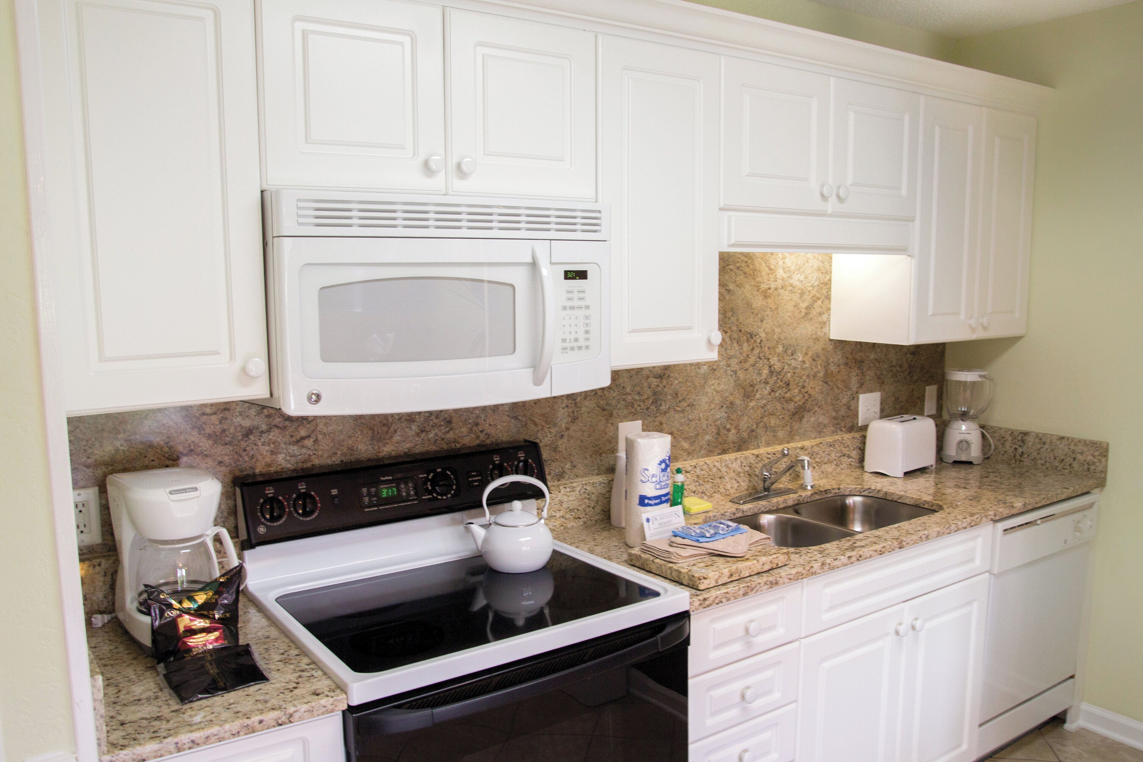 A kitchen with white cabinets, a microwave, stove, sink, and granite countertop.