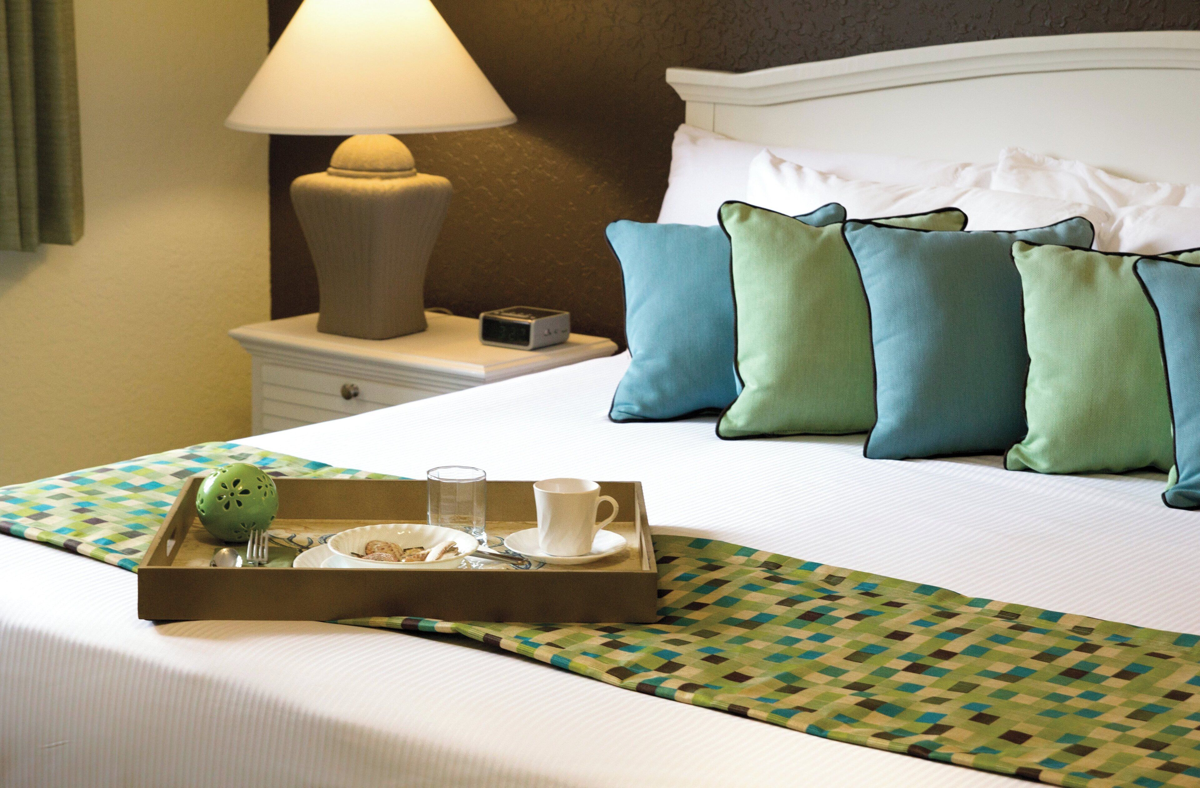 A neatly made bed with a tray of breakfast items, a bedside lamp, and a clock on a nightstand.