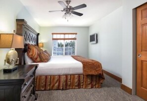 A bedroom with a bed, a ceiling fan, a window, and a door.