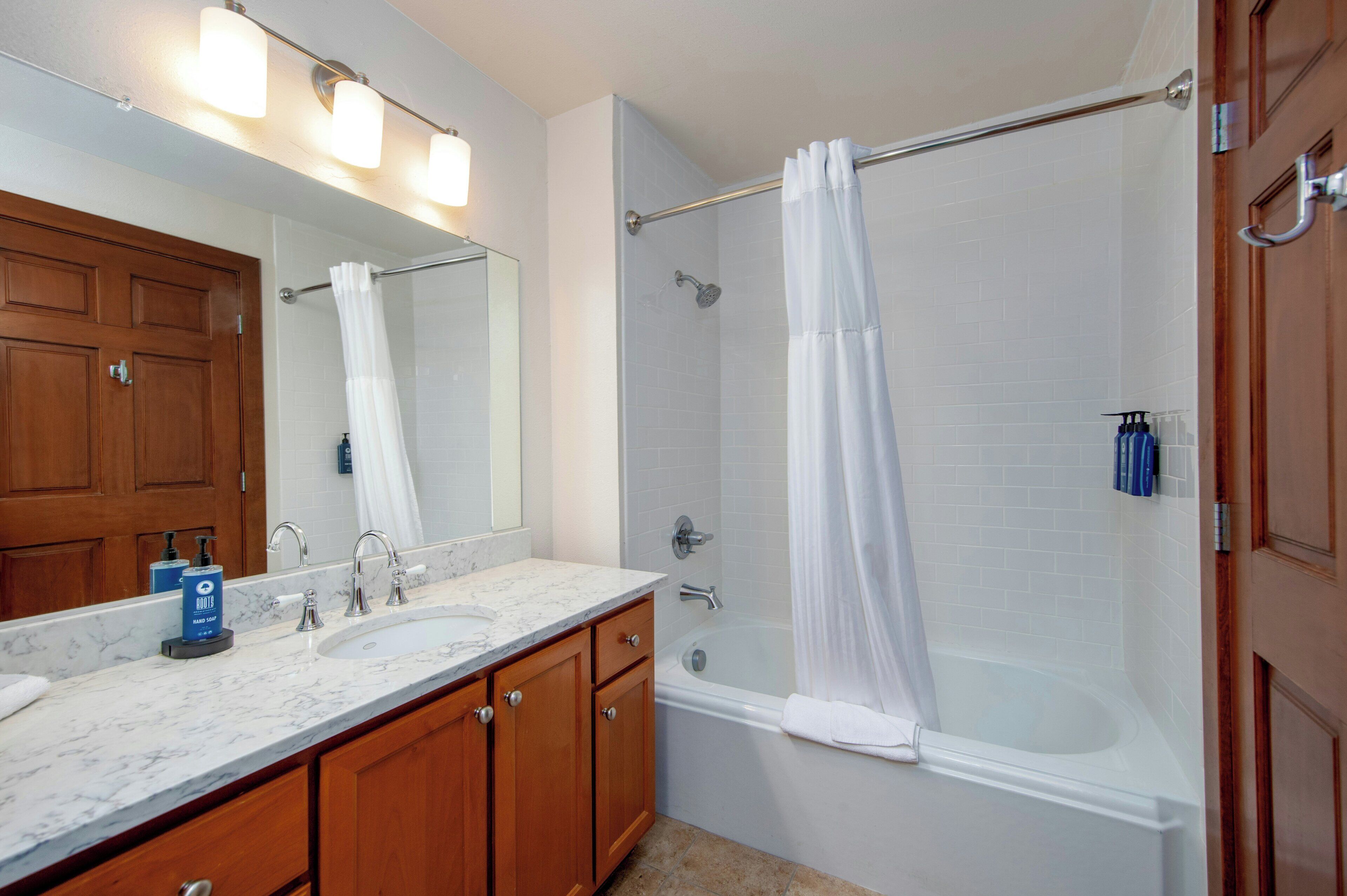 Une salle de bain avec deux éviers, une baignoire, un rideau de douche et un miroir avec éclairage intégré.