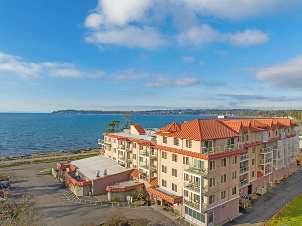 A multi-story hotel with balconies, a parking lot, and a view of the water.