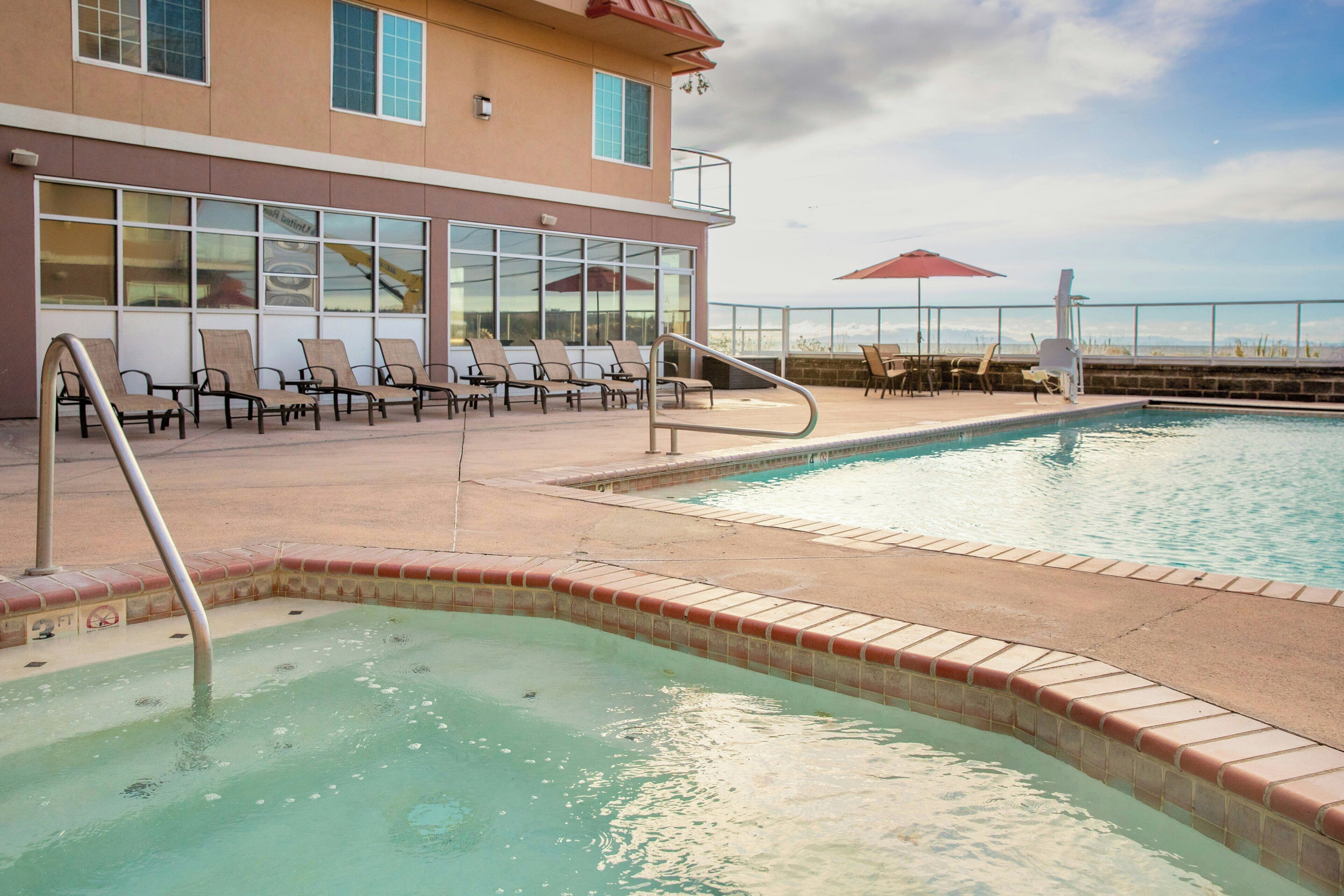 A pool area with lounge chairs and a building with large windows.