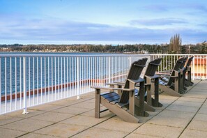 A waterfront seating area with chairs and a railing.