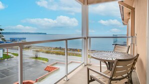 Ein Balkon mit Tisch und Stühlen, der auf ein Gewässer und eine entfernte Küstenlinie blickt.