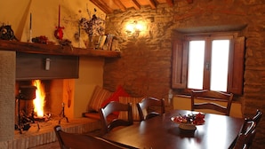 Un comedor acogedor con chimenea de piedra, mobiliario de madera y ventana con contraventanas.