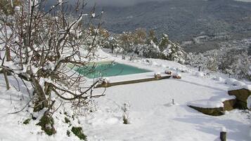 Paesaggio innevato con piscina e vista su colline lontane.