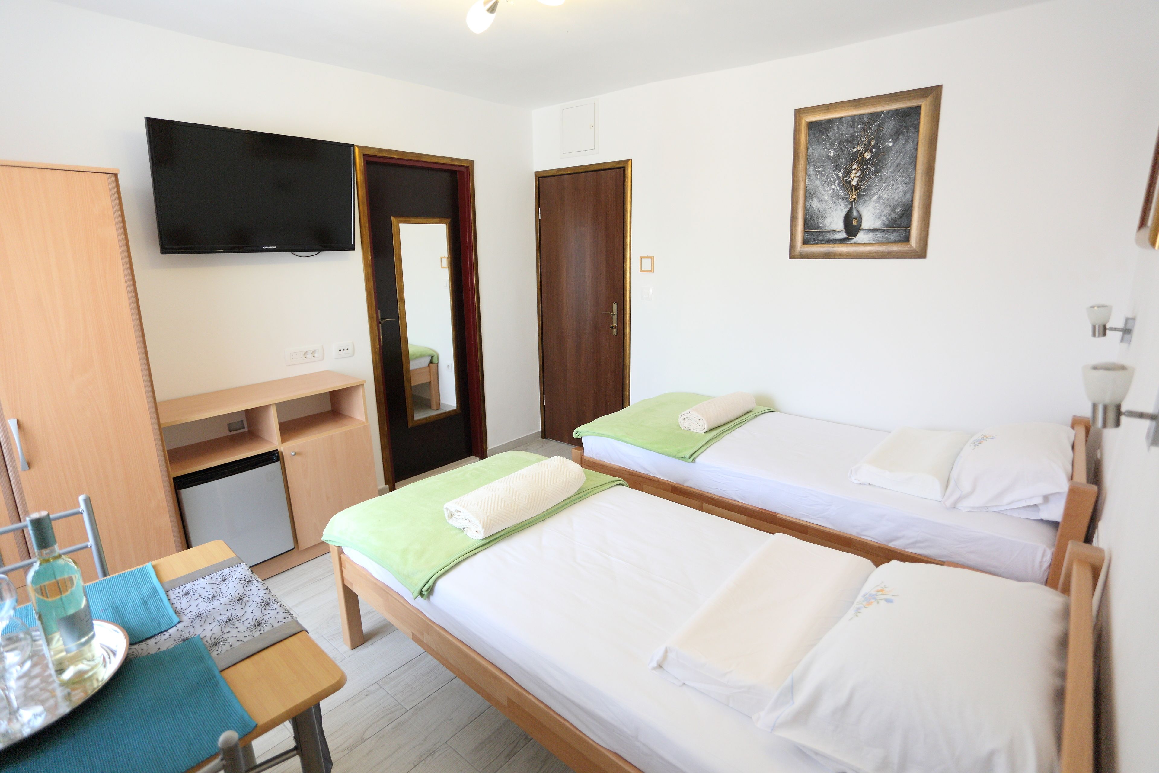 A hotel room with two single beds, a desk with a chair, a television, and a small refrigerator.