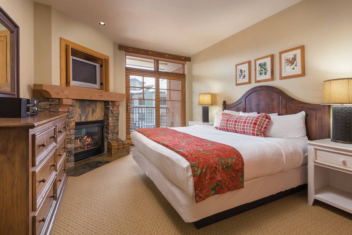 Un dormitorio con una cama grande, chimenea, televisor y cómoda.