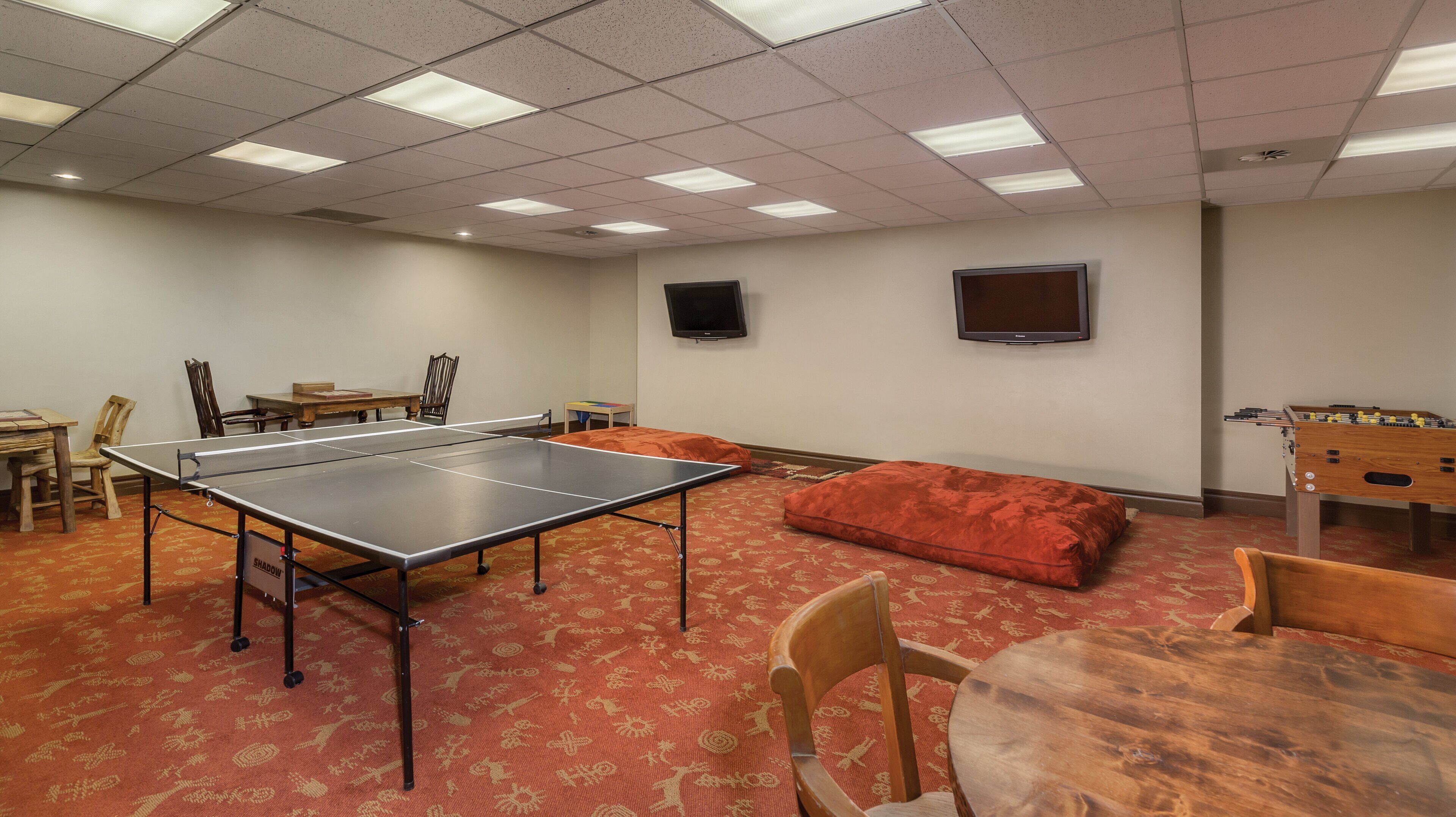 A room with a ping pong table, a foosball table, and a television mounted on the wall.