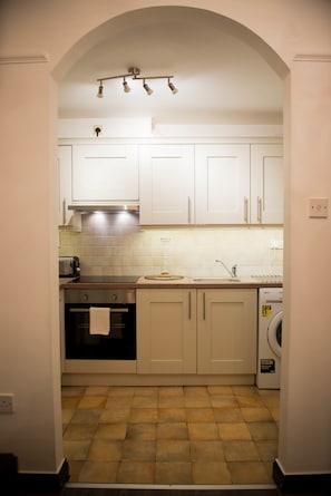 Una cocina compacta con armarios blancos, horno integrado, lavamanos y lavadora.