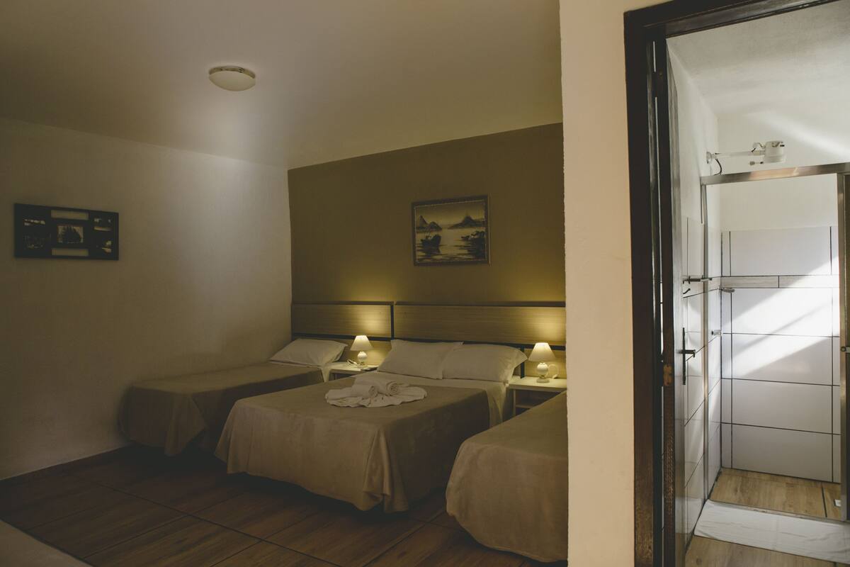 A hotel room with two single beds, a bedside table with a lamp, a framed picture on the wall, and a view of the bathroom.