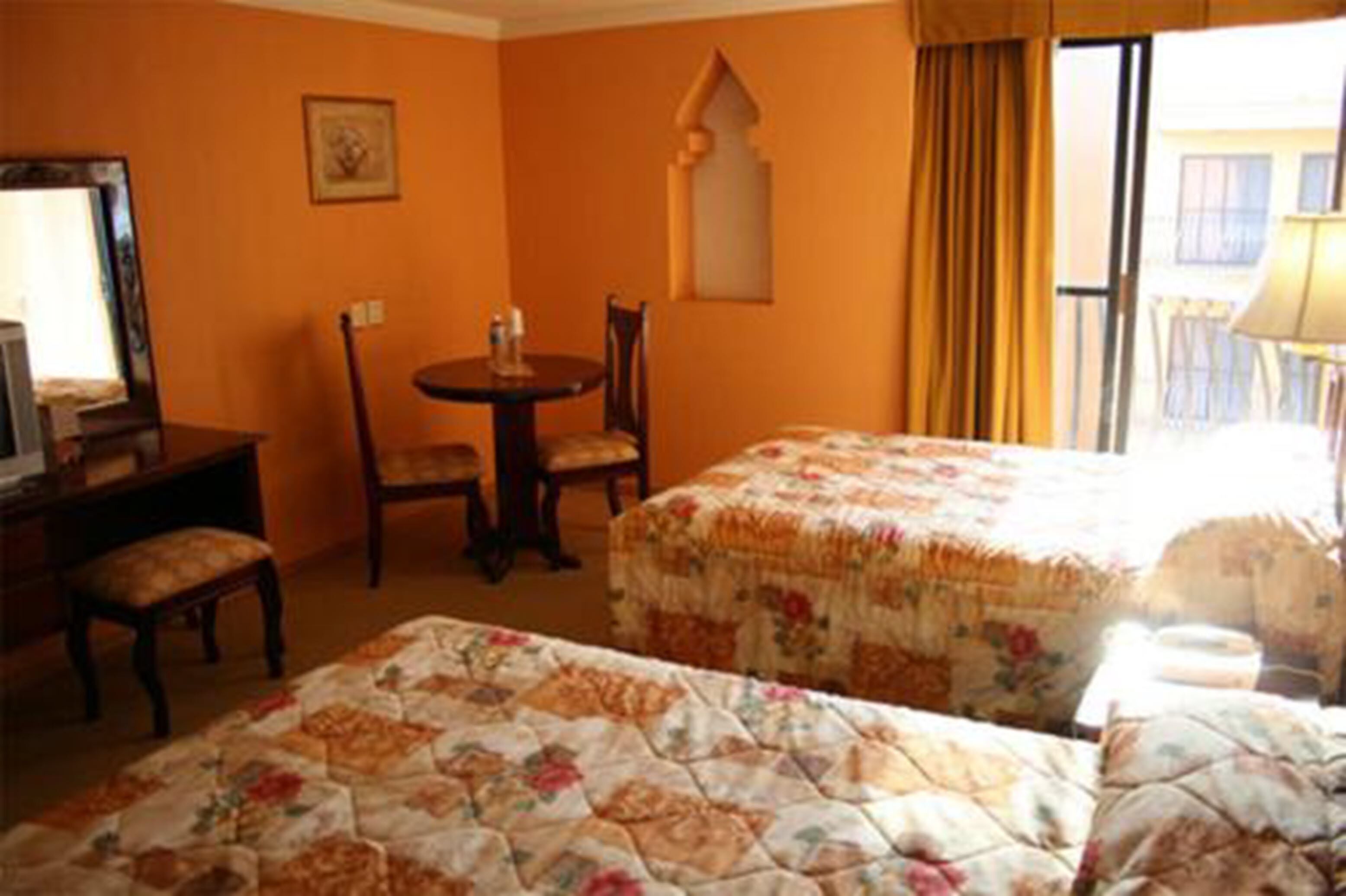 A hotel room with two beds, a desk, a chair, and a window with curtains.