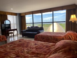 Habitación de hotel con un ventanal grande, un sofá, una cama con cubrecolcha estampado, un televisor y una lámpara.