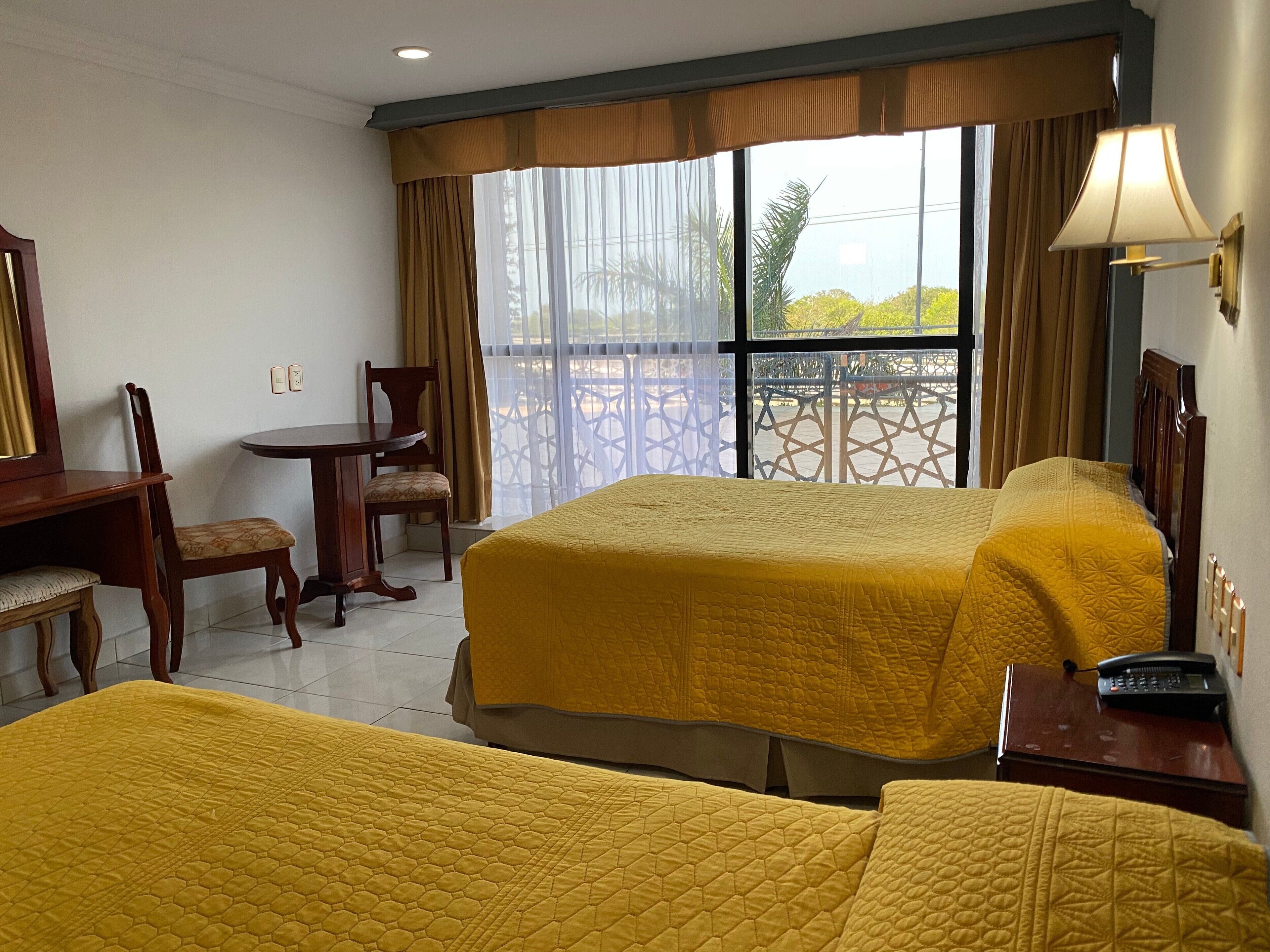 A hotel room with two beds, a desk, a chair, and a balcony with a view.