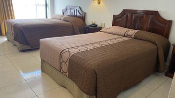 Dos camas matrimoniales con ropa de cama marrón, una mesita de noche con lámpara y un aplique de pared.