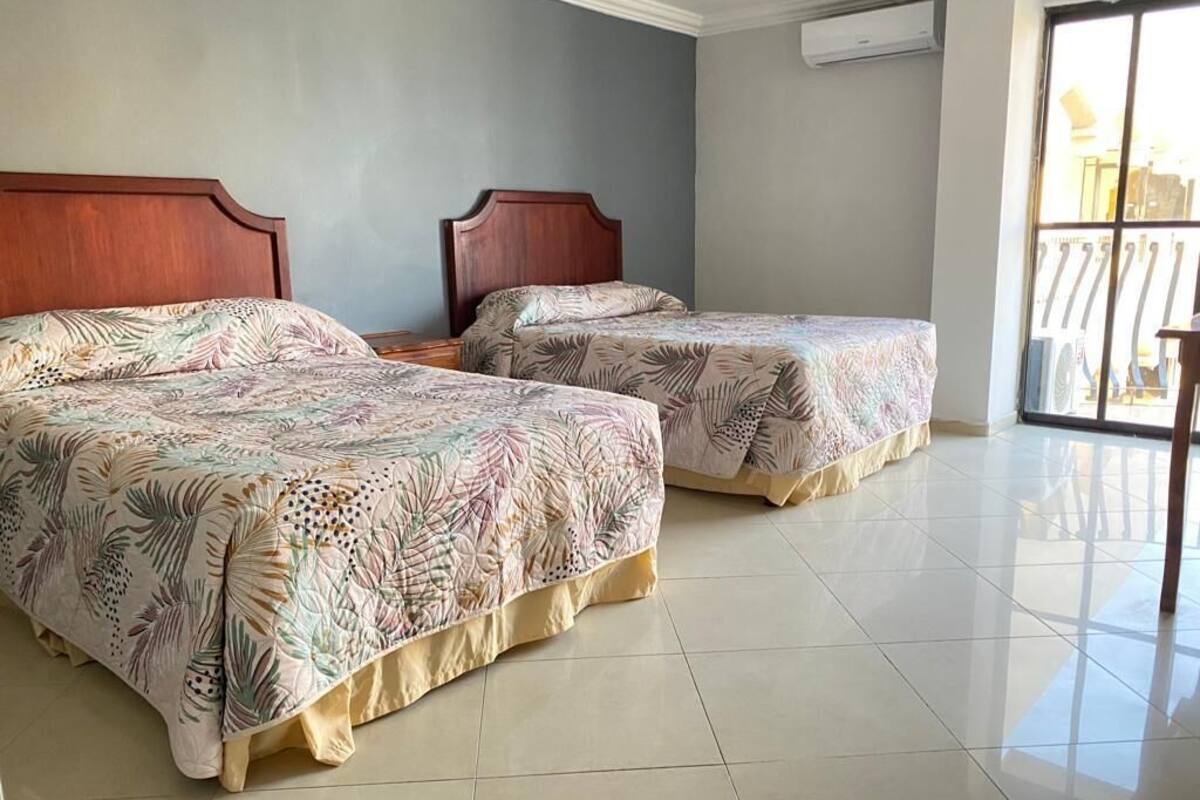 Una habitación de hotel con dos camas, un ventanal grande y piso de baldosas.