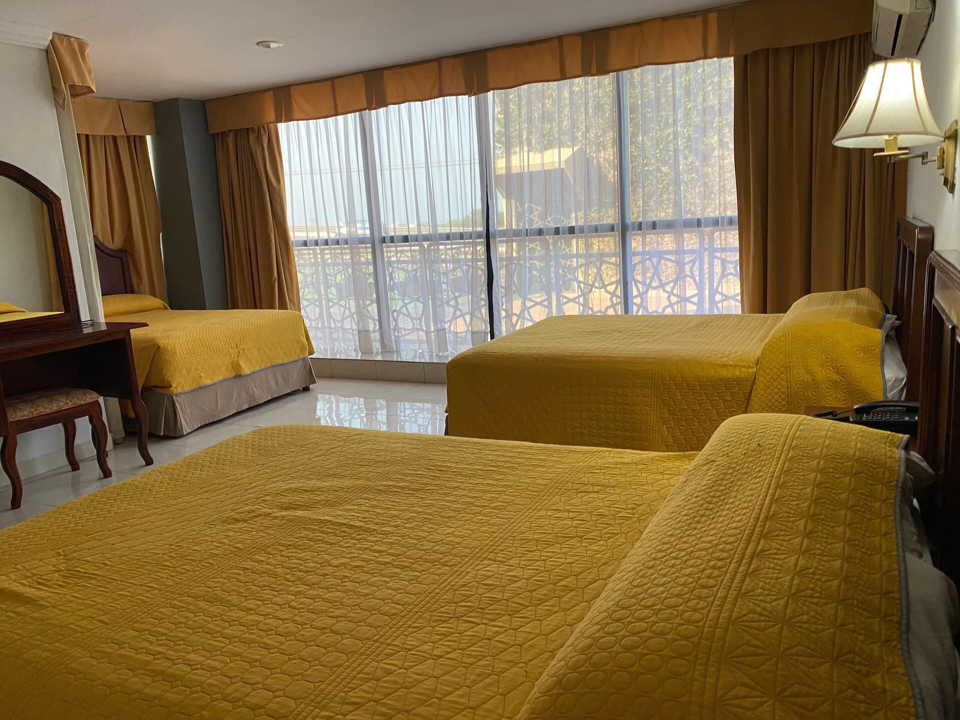 A hotel room with two beds, a desk, a chair, and a window with curtains.