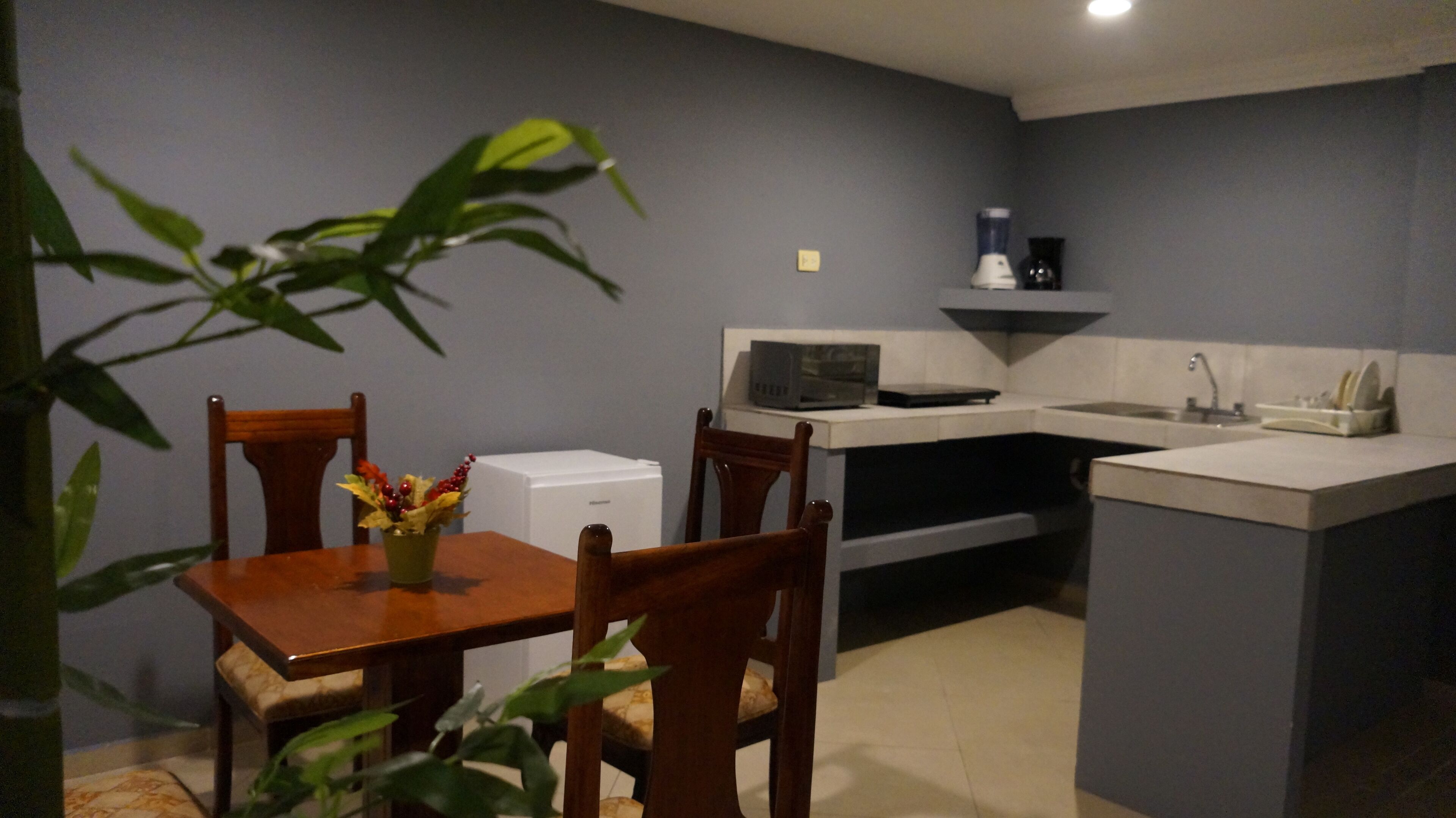 A compact kitchen with a dining table, chairs, a microwave, a coffee maker, and a small refrigerator.