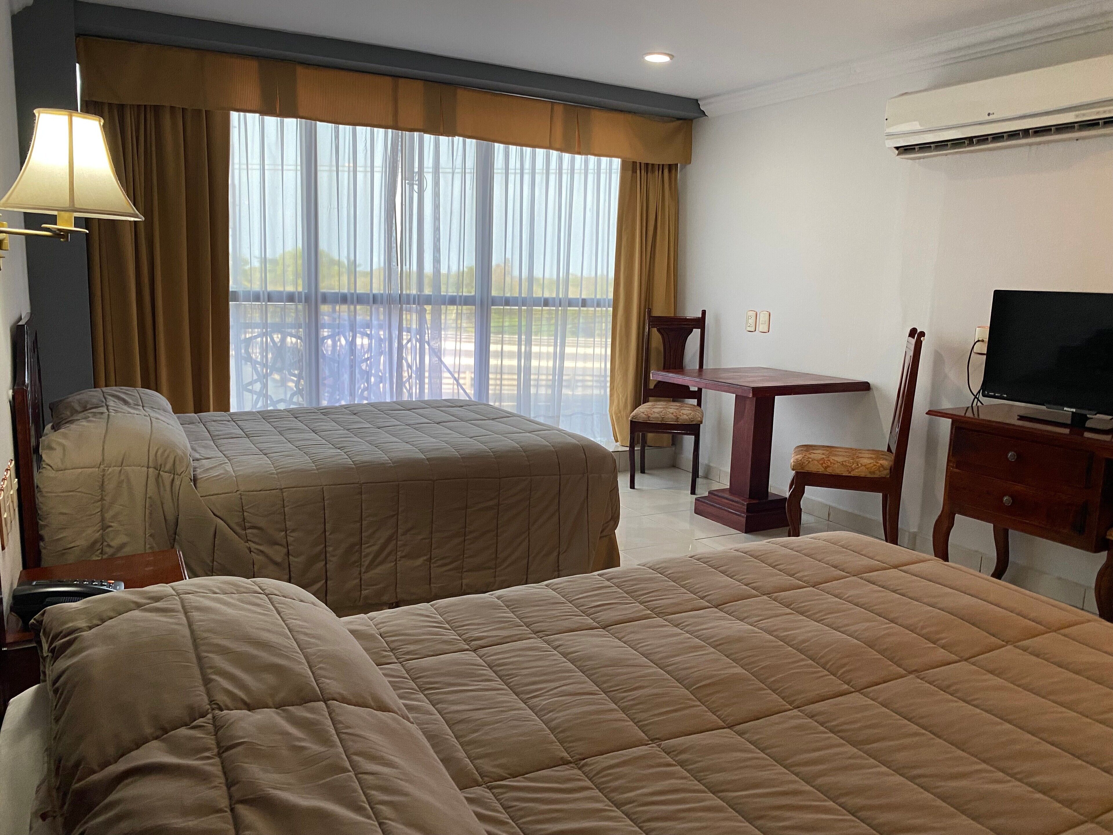 A hotel room with two beds, a desk, a chair, a television, and a window with curtains.
