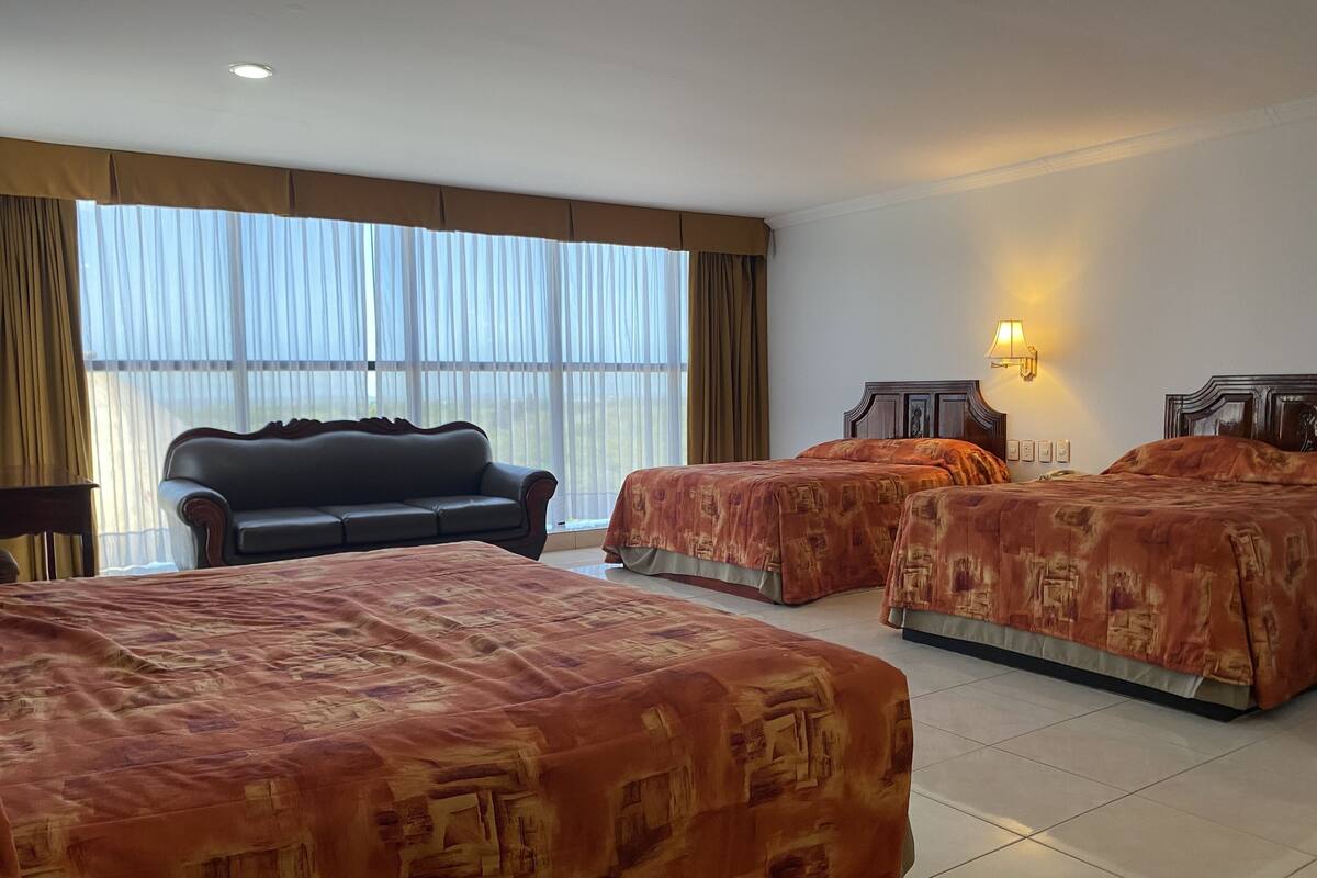 Habitación de hotel con dos camas, un sofá y un ventanal con cortinas.