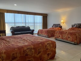 A hotel room with two beds, a sofa, and a large window with curtains.