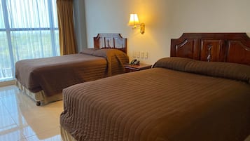 Una habitación de hotel con dos camas, una mesita de noche con lámpara y una ventana con cortinas.
