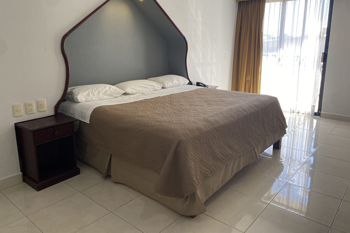 Una habitación de hotel con una cama grande, una mesita de noche y una ventana con cortinas.