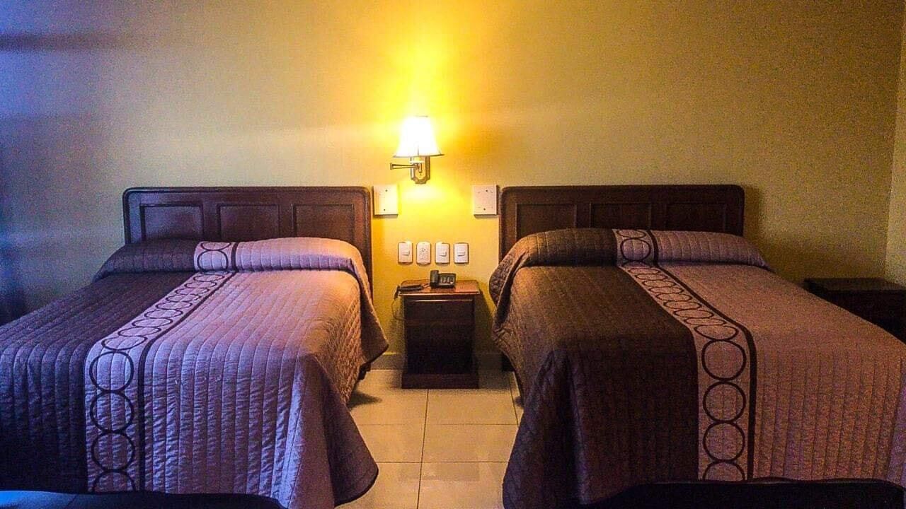 Een hotelkamer met twee eenpersoonsbedden, een nachtkastje met een lamp, en een wandlamp.