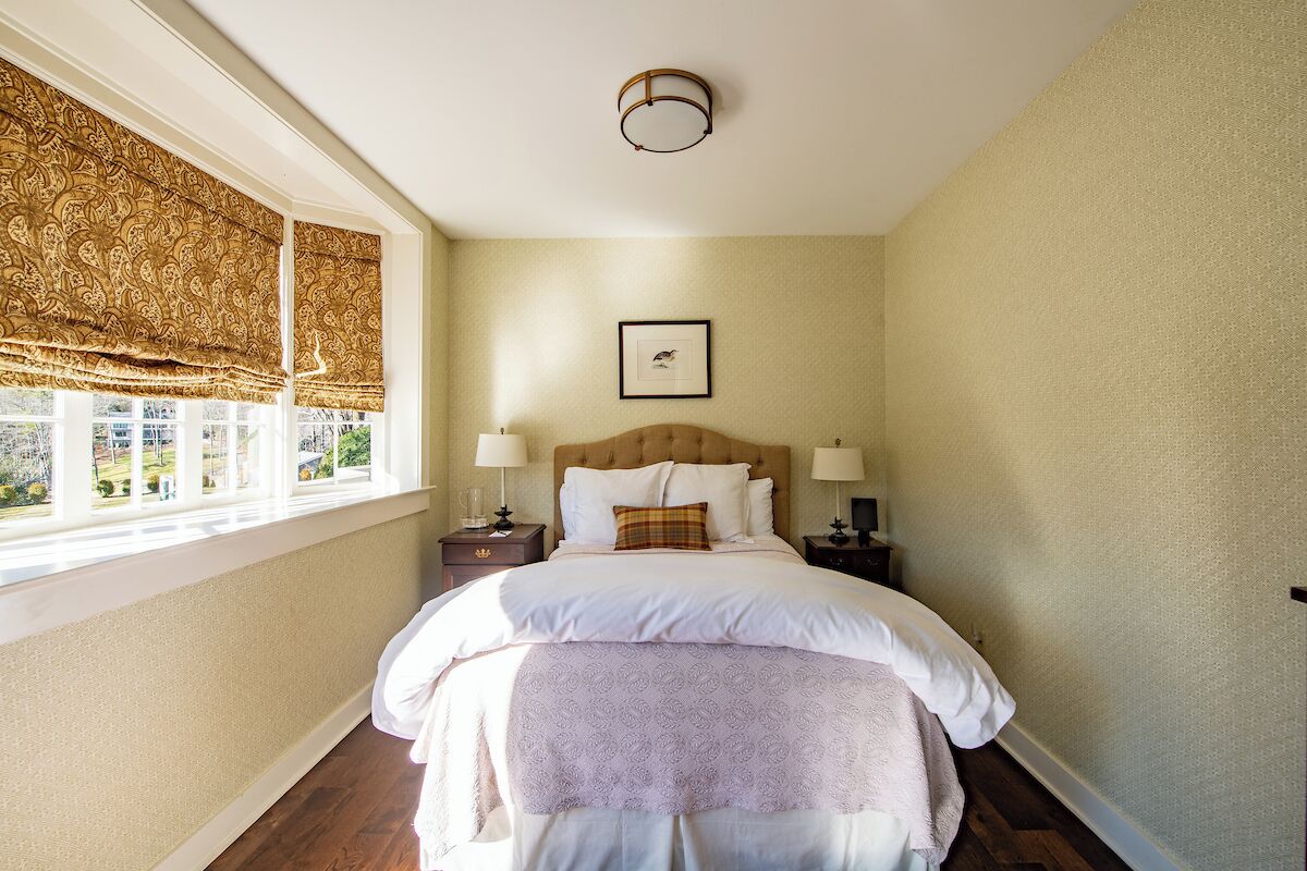 Ein Schlafzimmer mit großem Fenster, einem Bett mit weißer Bettwäsche, zwei Nachttischen mit Lampen und einem gerahmten Bild an der Wand.