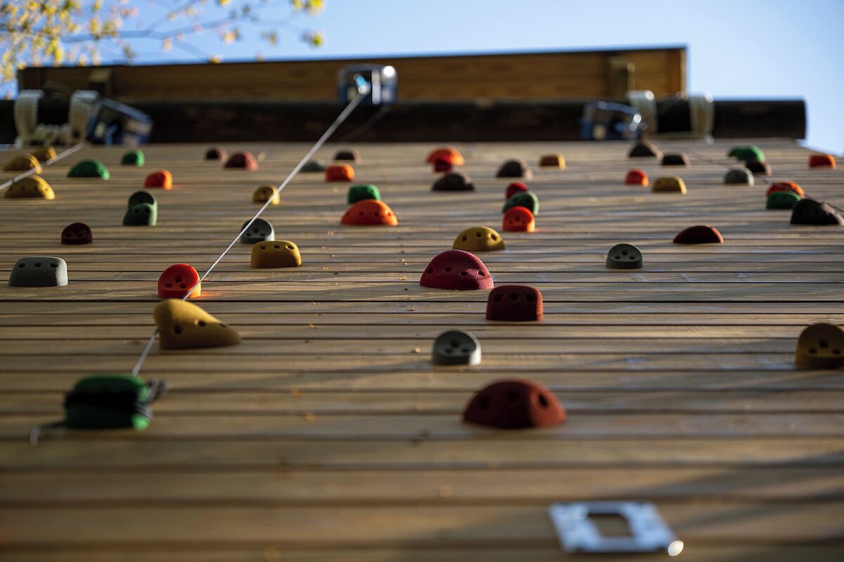 Una pared de escalar con elementos de colores variados y un palo para selfies en primer plano.