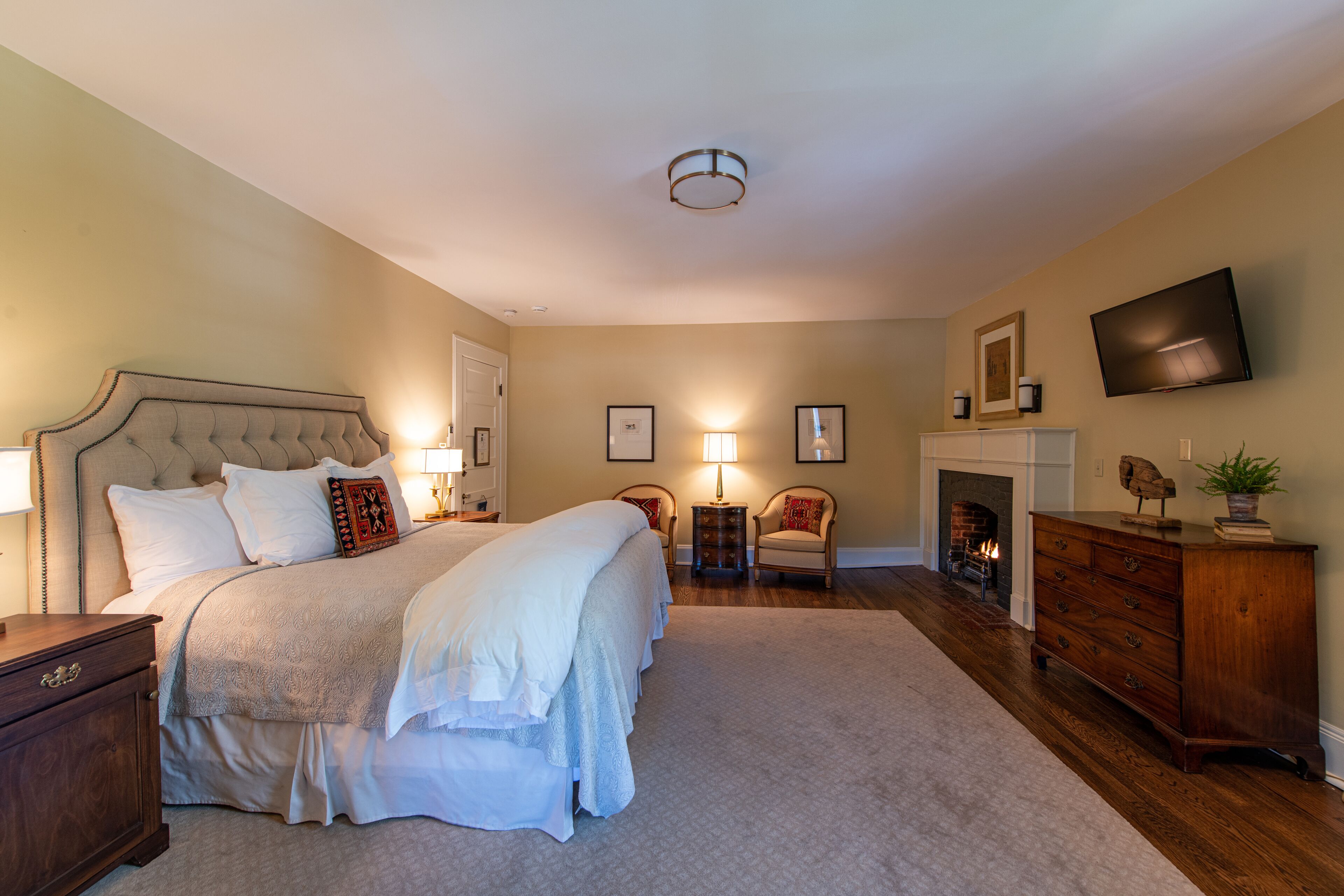 A bedroom with a large bed, bedside tables, a dresser, a TV, and a fireplace.