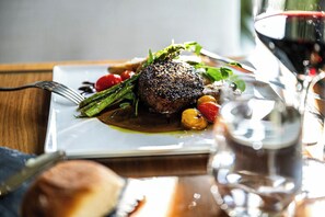 A plated dish with a steak, asparagus, and cherry tomatoes, accompanied by a glass of red wine.