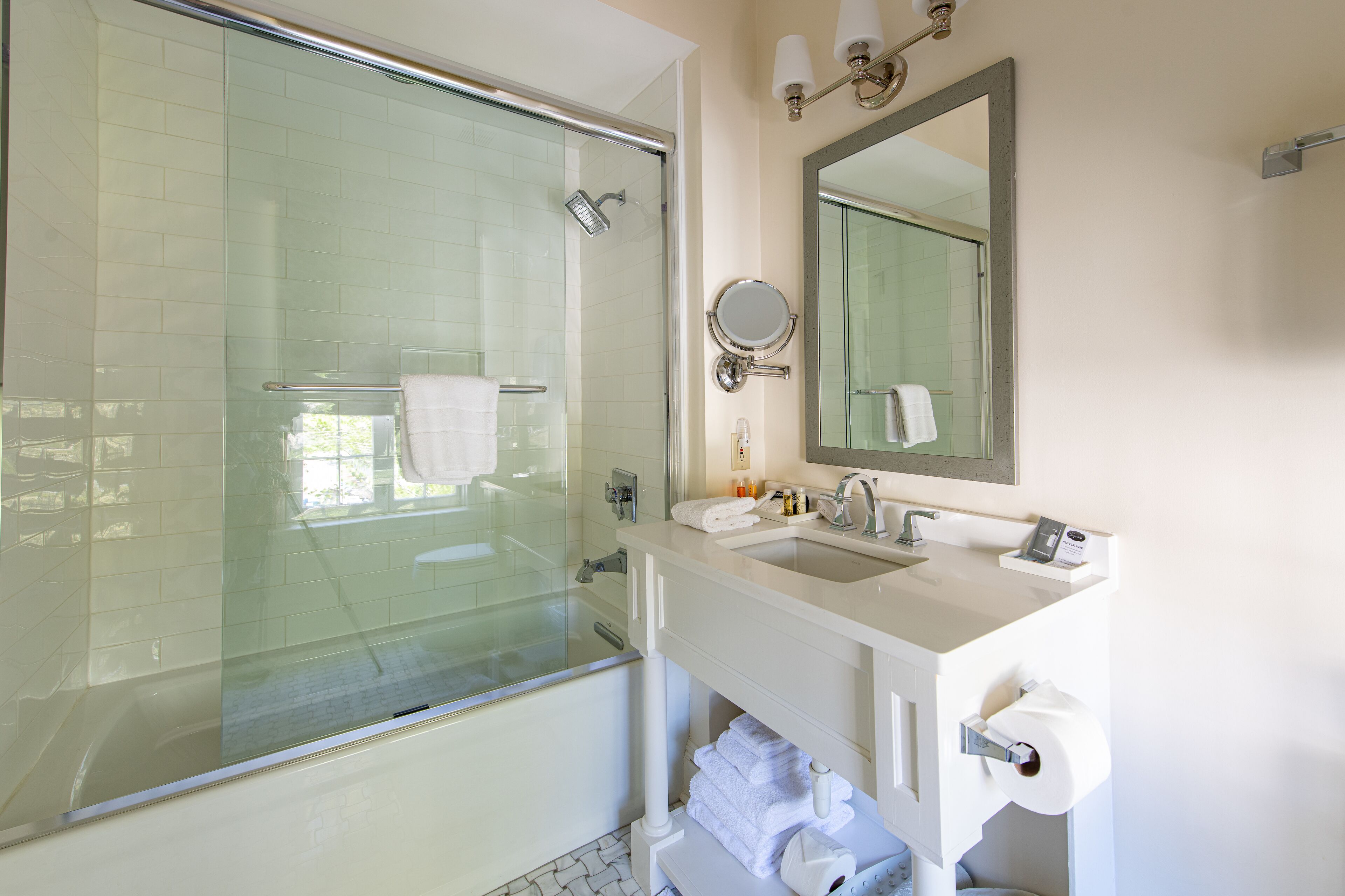 A modern bathroom with a glass-enclosed shower, a sink with a mirror, and neatly stacked towels.