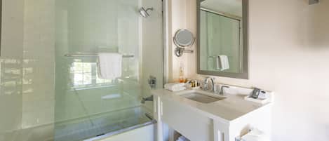 A modern bathroom with a glass-enclosed shower, a sink with a mirror, and neatly stacked towels.