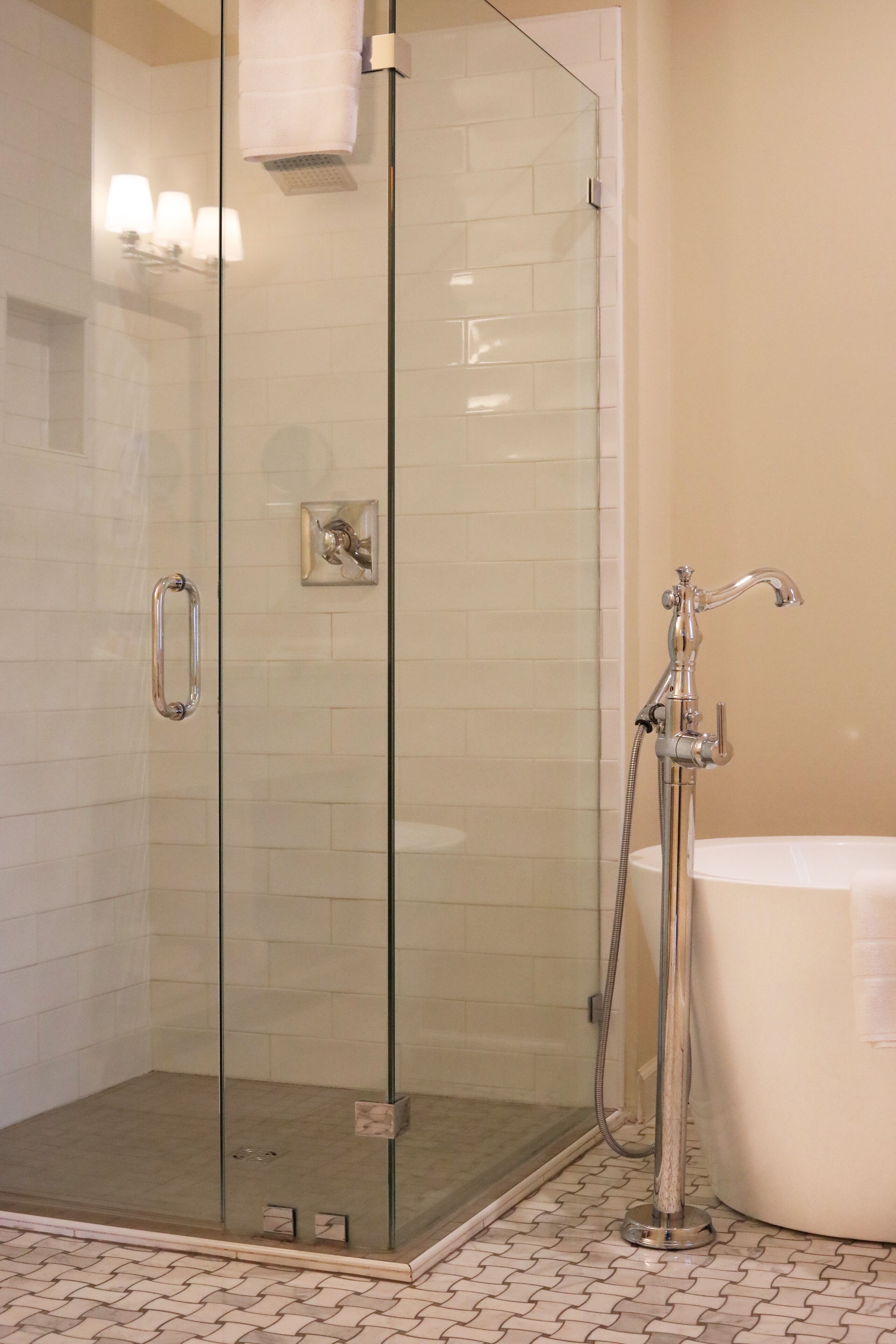 A glass-enclosed shower with a handheld showerhead, a glass door handle, and a tiled floor.